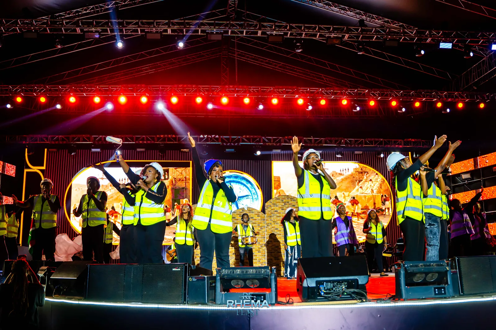 The R Collective performing in hard hats and high-visibility vests, staging the work of rebuilding