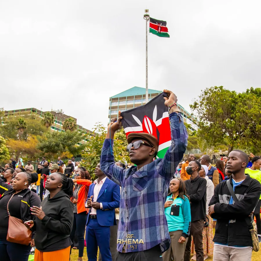 A worshipper's hand raised, a Kenyan flag draped over their shoulders