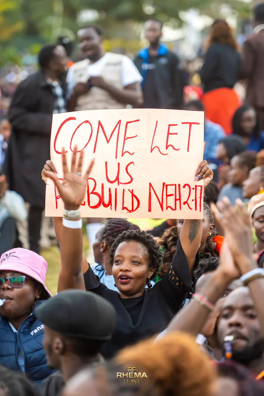 A hand-lettered placard reading Come Let Us Rebuild, Neh 2:17, held up in the crowd