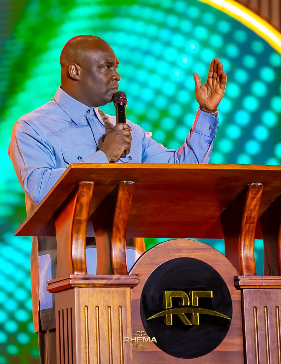 Apostle Joshua Selman with one hand raised at the pulpit