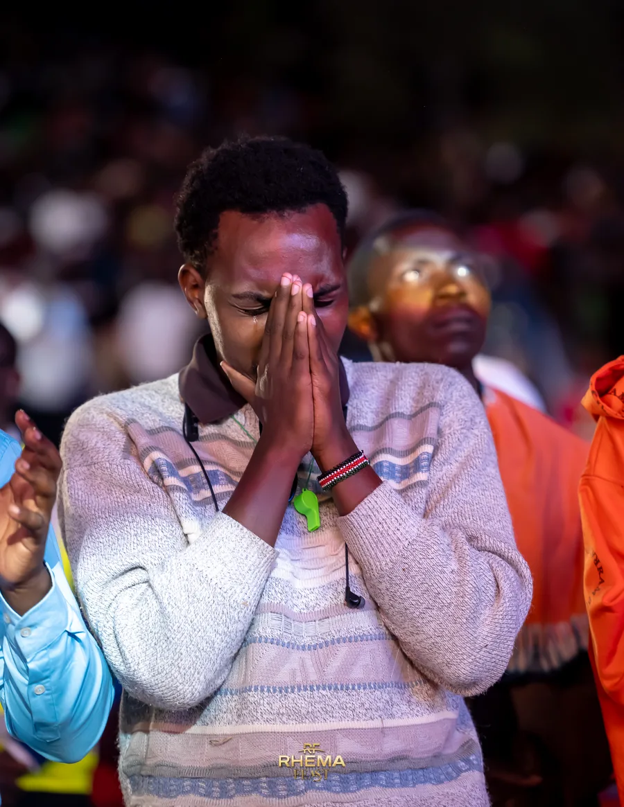 A woman in the crowd with her hands pressed together in prayer